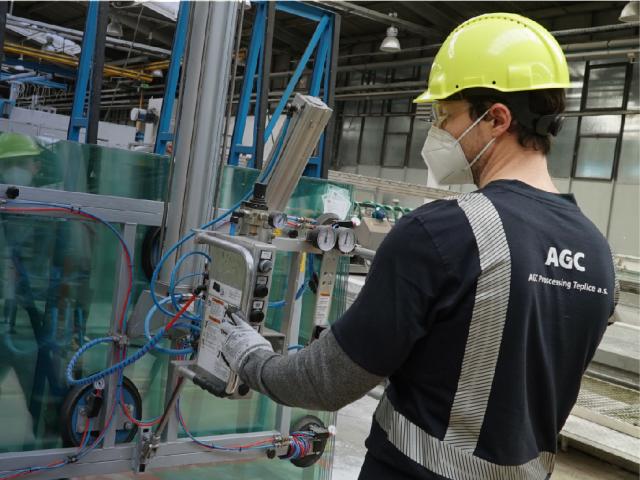 A man works in a AGC factory wearing a hard hat, a mask and protective goggles