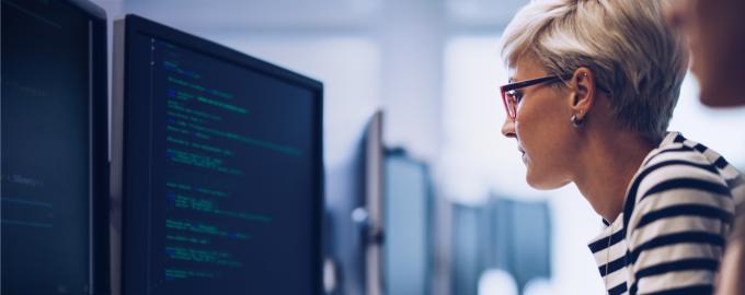 A blonde woman with short hair wearing glasses is busy working at a computer